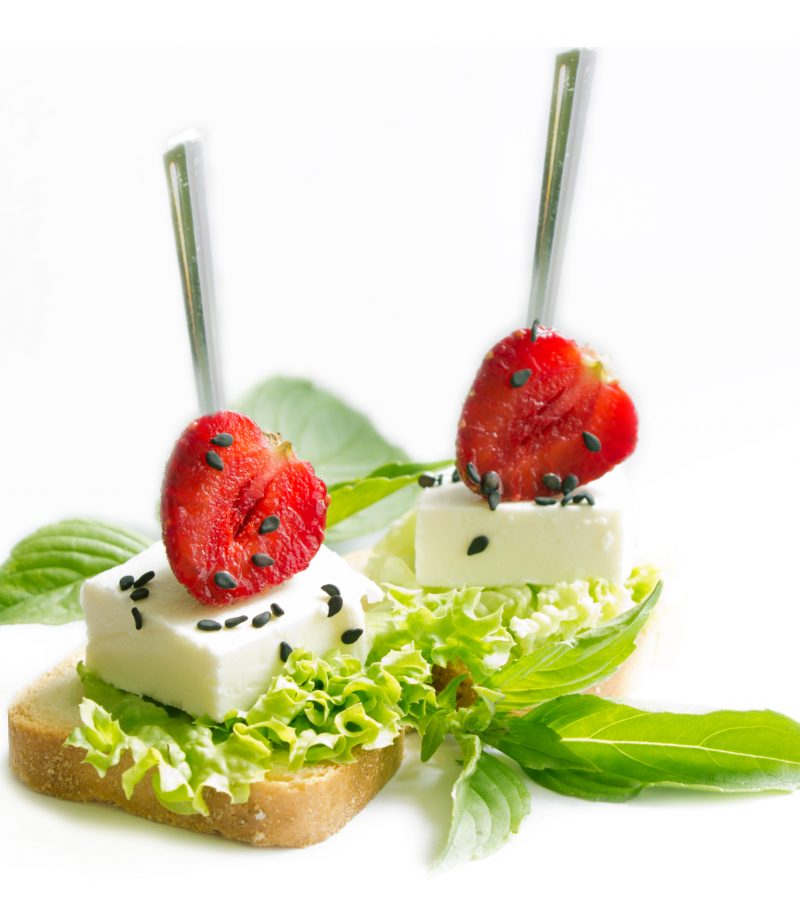 Delicious canapes wiyh feta cheese , strawberrys black sesame  and fresh basil leaves isolated on white